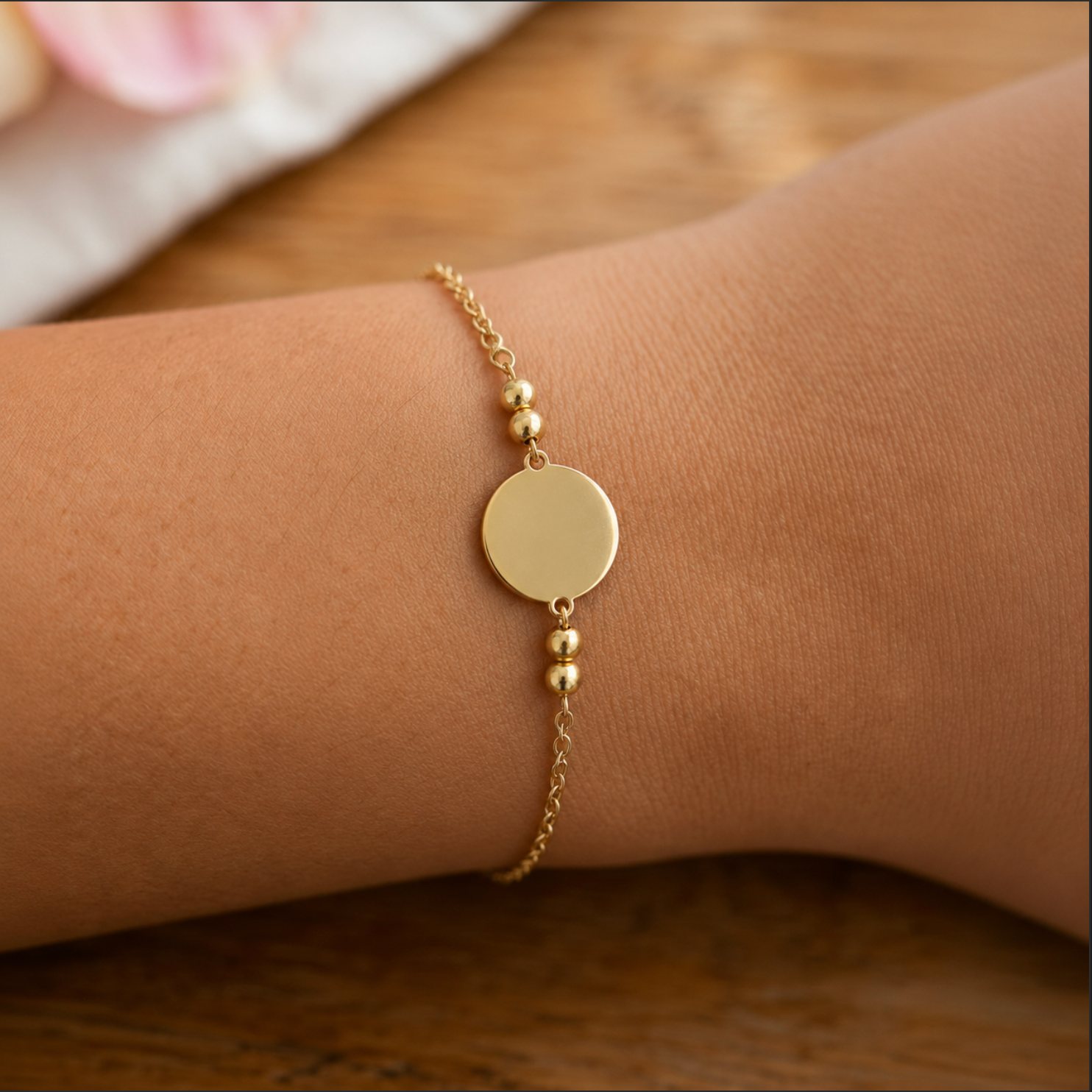 Gold bracelet with round charm on a wrist against a wooden background